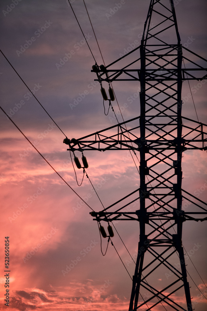 High voltage power lines pylons and electrical cables on a sunset sky background. Modern infrastructure of high voltage transmission lines. Overhead power lines towers equipment. Energy industry.