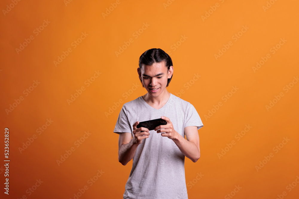 Excited teen playing video games on phone, young asian man having fun, enjoying online mobile videogames. Internet leisure activity, cheerful gamer using smartphone entertainment application Excited teen playing video games on phone, young asian man having fun, enjoying online mobile videogames. Internet leisure activity, cheerful gamer using smartphone entertainment application