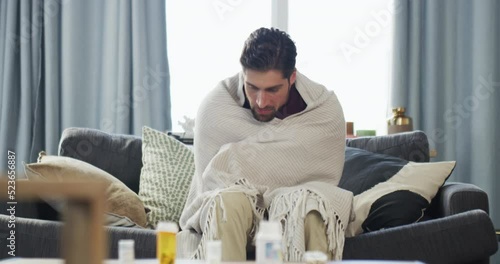Sick, cold and tired young man with a fever sitting at home on sofa. Man showing symptoms of a flu, illness or virus in isolation shivering and feeling unwell having health problems. photo