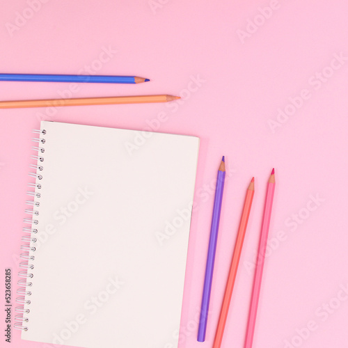 PAstel wooden pencils with open notebook copy space on pastel pink background. Flat lay