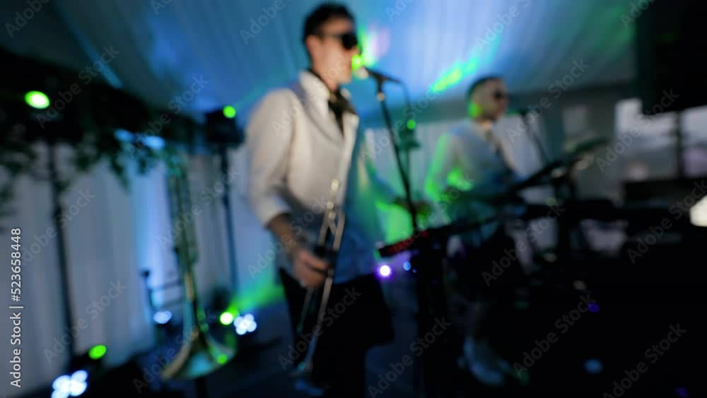Blurry: Band is performing at a nightclub singing and playing on instruments Blurry: Band is performing at a nightclub singing and playing on instruments