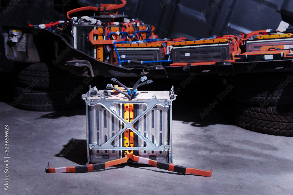 Naklejka premium Electric car lithium power cell with power connections in front of maintained car battery. Blue toned. EV car battery at maintenance.