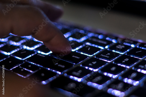 Finger pressing Enter key close up on backlit keyboard.  Computer keyboard, laptop keyboard. 