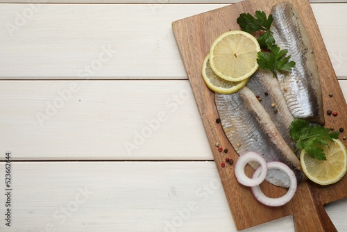 Delicious salted herring fillets served with lemon, parsley and onion rings on white wooden table, top view. Space for text