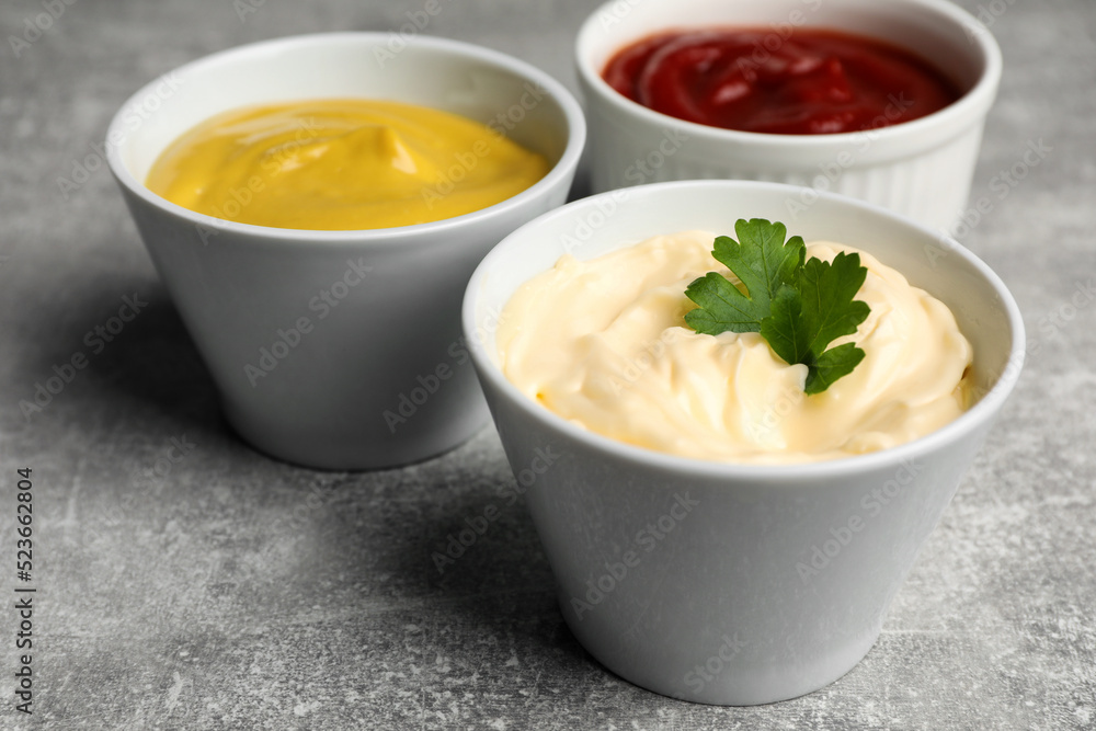 Bowls with mustard, ketchup and mayonnaise on light grey table, closeup Bowls with mustard, ketchup and mayonnaise on light grey table, closeup