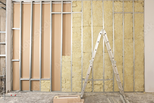 Ladder near wall with metal studs and insulation material indoors photo