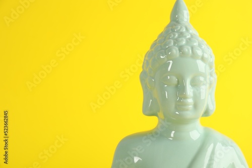 Beautiful ceramic Buddha sculpture on yellow background. Space for text