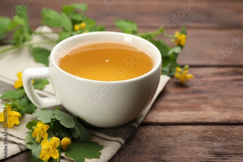 Cup of aromatic celandine tea and flowers on wooden table, closeup