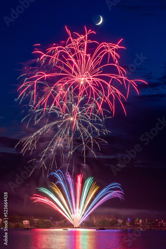 Fireworks celebration with reflections across the river with a town in the background