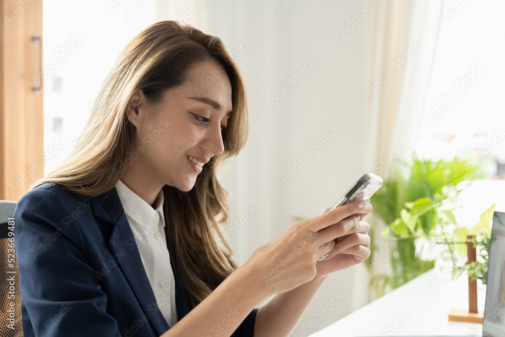 Smiling businesswoman using phone in office. Small business entrepreneur looking at her mobile phone and smiling. Smiling businesswoman using phone in office. Small business entrepreneur looking at her mobile phone and smiling.