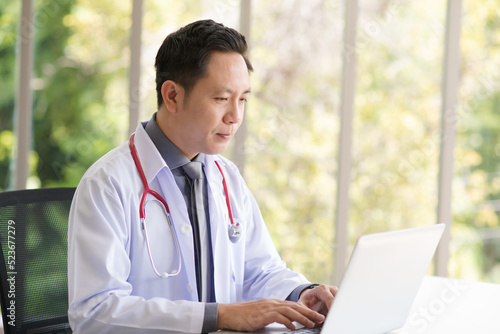 Asian Doctor man sitting and using laptop in modern workplace office.