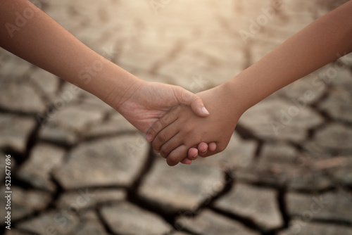 Foto Young boy and girl holding hands on cracks in the dried soil in arid season