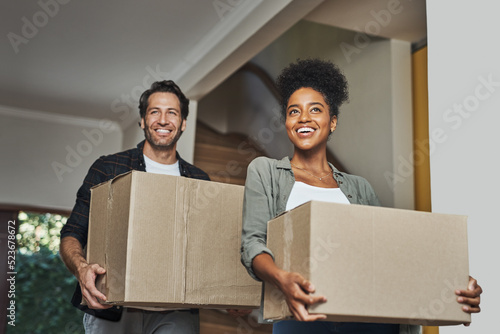 New house, moving and happy couple carrying boxes while feeling proud and excited about buying a house with a mortgage loan. Interracial husband and wife first time buyers unpacking in dream home photo