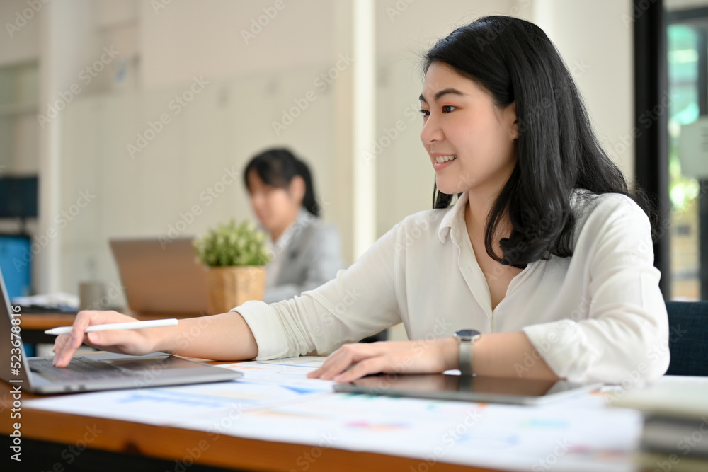 Asian businesswoman or employee at her office desk, using laptop. Asian businesswoman or employee at her office desk, using laptop.