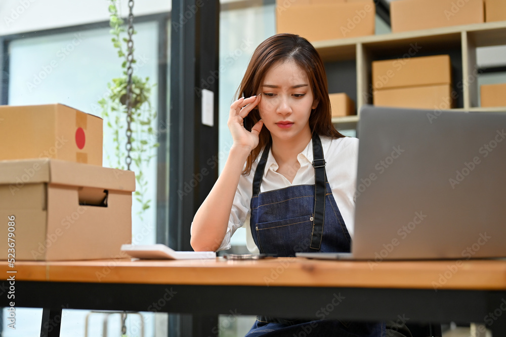 Stressed Asian female online startup business working at her office desk in stock room Stressed Asian female online startup business working at her office desk in stock room