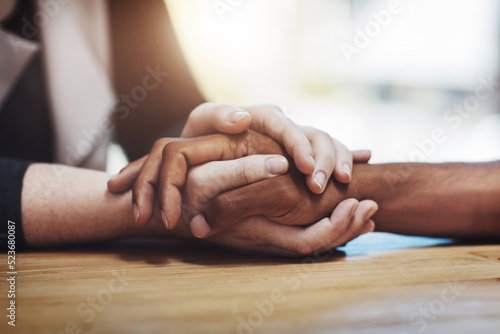 Support, compassion and trust while holding hands and sitting together at a table. Closeup of a loving, caring and interracial couple or friends comforting each other after a loss or cancer news