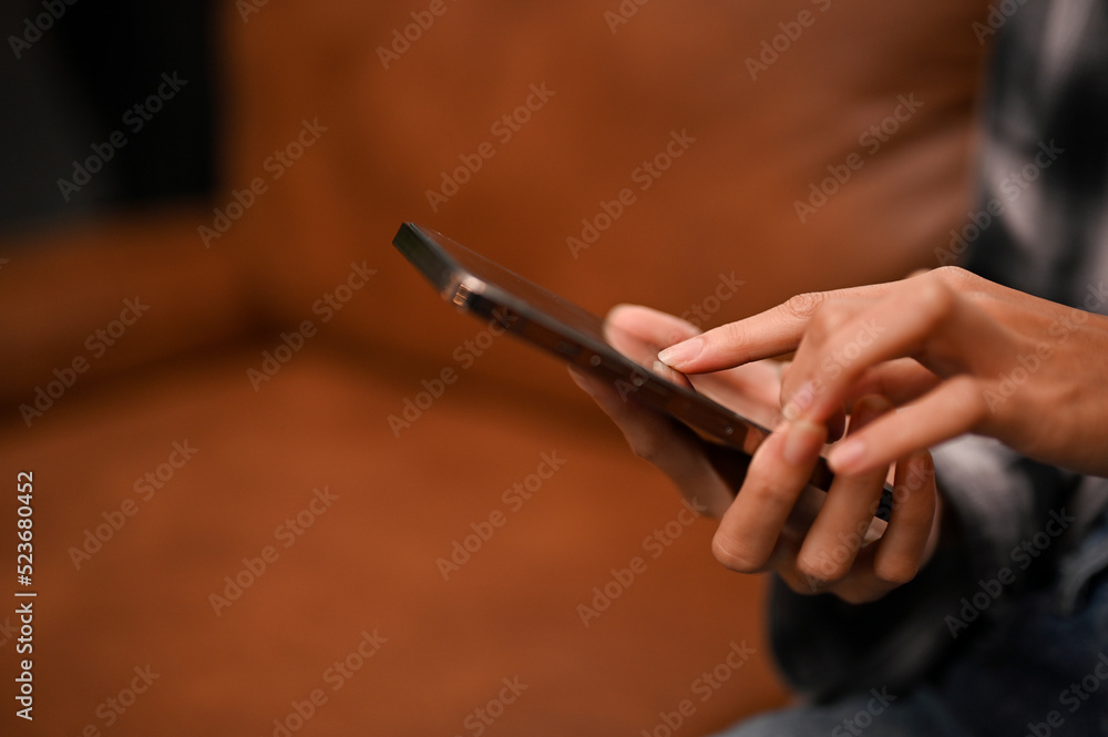 A female hands holding a smartphone over blurred modern living room in the background.