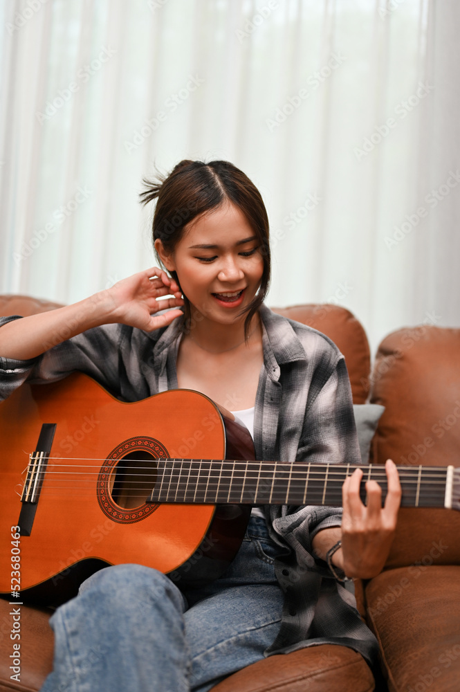 Portrait, An attractive Asian female is on the sofa, singing and playing guitar.