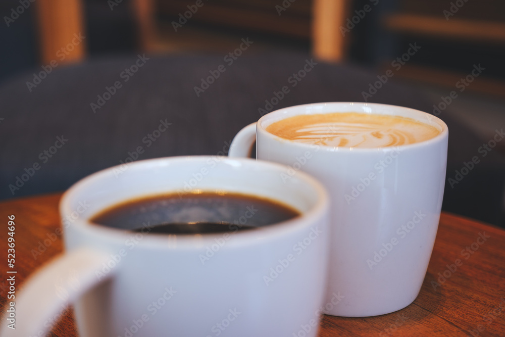 Closeup image of two white cups of hot coffee on wooden table in cafe Closeup image of two white cups of hot coffee on wooden table in cafe