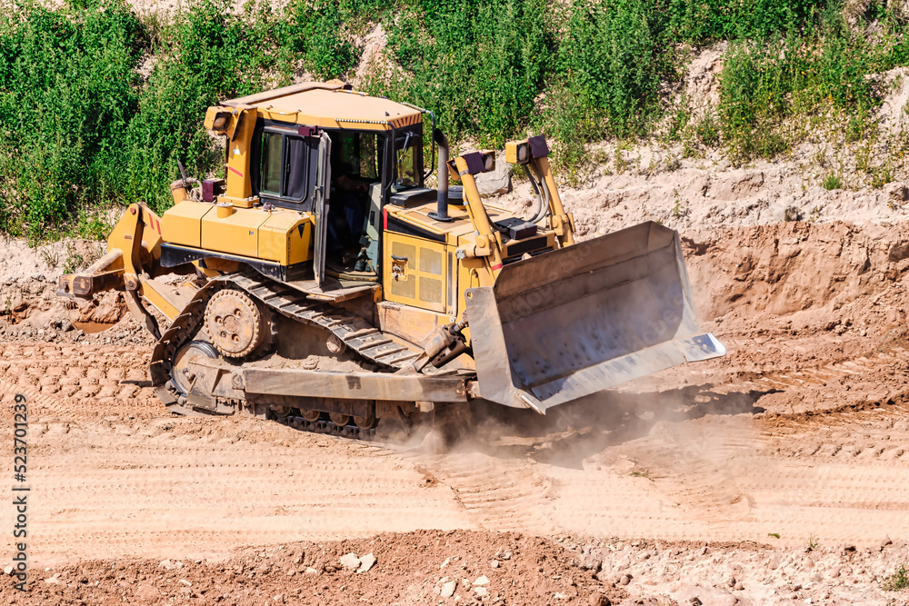 A powerful bulldozer in a sand pit is planning a site. Extraction of sand in an open pit. natural building materials. A powerful bulldozer in a sand pit is planning a site. Extraction of sand in an open pit. natural building materials.