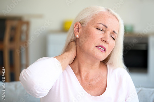 Mature woman suffering from neck pain in kitchen, closeup