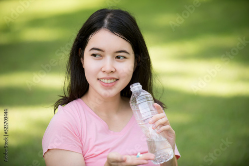 Happy pregnant Asian woman sitting on lawn and drinking water. Pregnancy, motherhood, people and expectations.