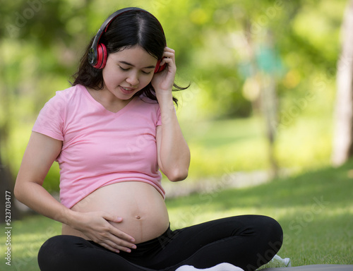 We love music, beautiful pregnant woman holding headphones on her stomach while leisurely sitting in the park with her new dad.