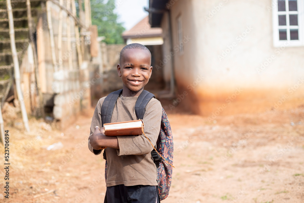 Fototapeta premium An African boy student wearing bag pack and holding school books smiling and looking at camera
