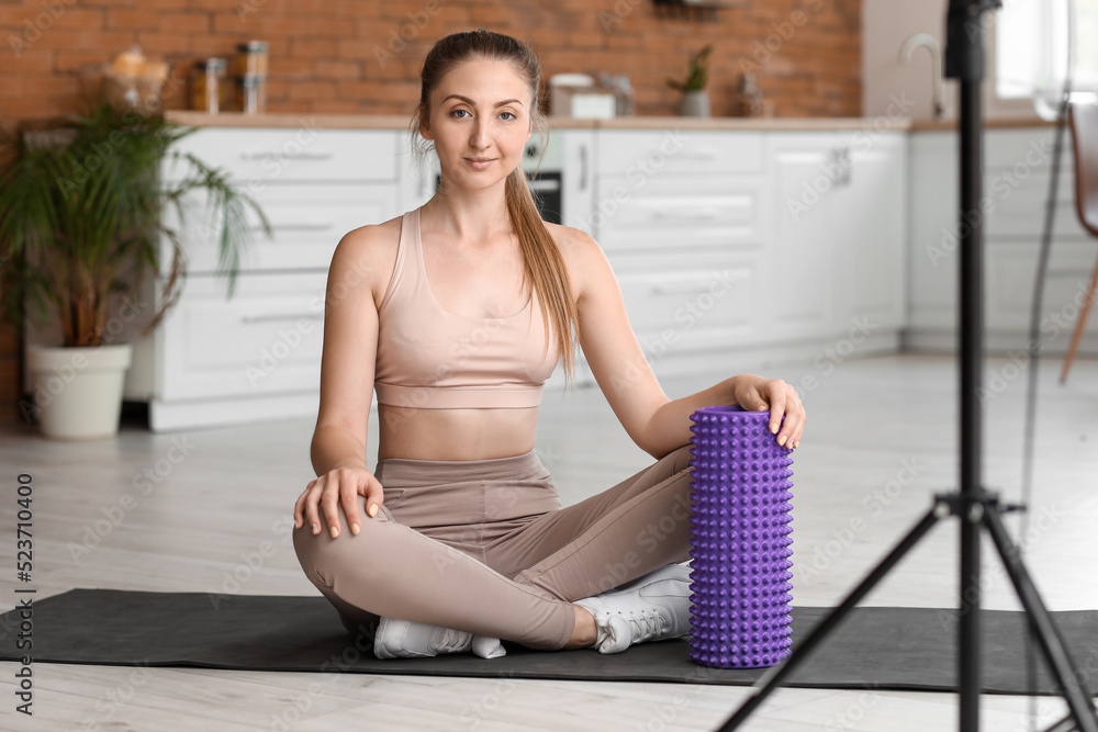 Young woman with foam roller recording video in kitchen Young woman with foam roller recording video in kitchen