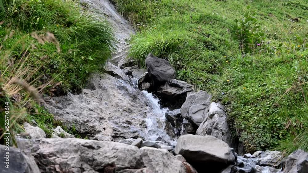 A hiker jumps across a small glacier stream in the Swiss Alps, splashing water. Engelberg, Obwalden A hiker jumps across a small glacier stream in the Swiss Alps, splashing water. Engelberg, Obwalden