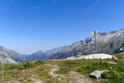 Scenic view of mountain panorama with hiking trail sign post seen from summit of Swiss mountain pass Grimsel on a sunny summer day. Photo taken July 3rd, 2022, Grimsel Pass, Switzerland.