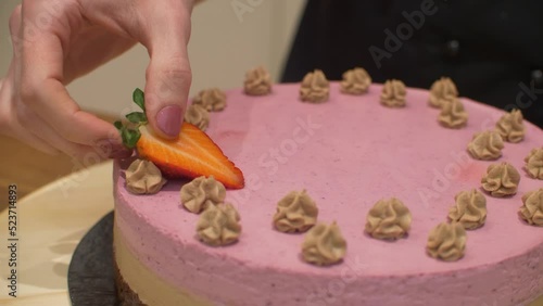 Woman decorating cream cake with strawberries on spinning plate. Close up of confectioner woman putting half of strawberrie on delicious creamy cake for birthday celebration. photo