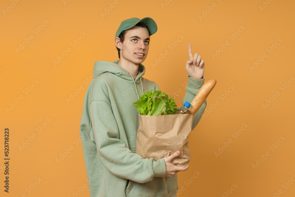 food delivery man holding a paper bag with fresh products and pointing his finger up on a colored background with space for text food delivery man holding a paper bag with fresh products and pointing his finger up on a colored background with space for text