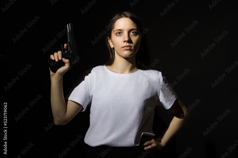 young woman with long hair in a white t-shirt holding a gun in her hand on a black background young woman with long hair in a white t-shirt holding a gun in her hand on a black background