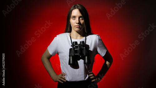 young beautiful woman with long hair in a white t-shirt with binoculars on a red background