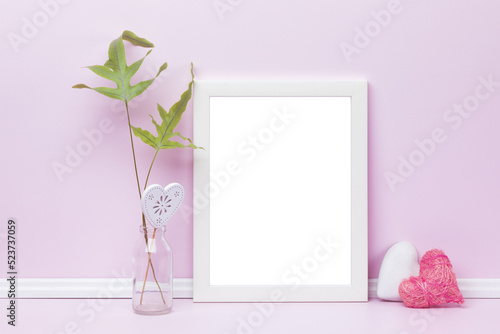Feminine picture frame mockup. Transparent template with white vertical frame, heart-shaped ornaments and fern leaves in front of pink wall