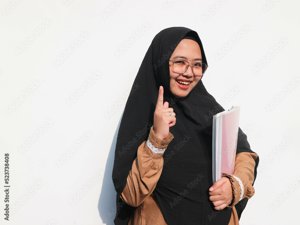 Portrait of beautiful Asian Muslim woman holding book while pointing finger, Isolated on white background Portrait of beautiful Asian Muslim woman holding book while pointing finger, Isolated on white background