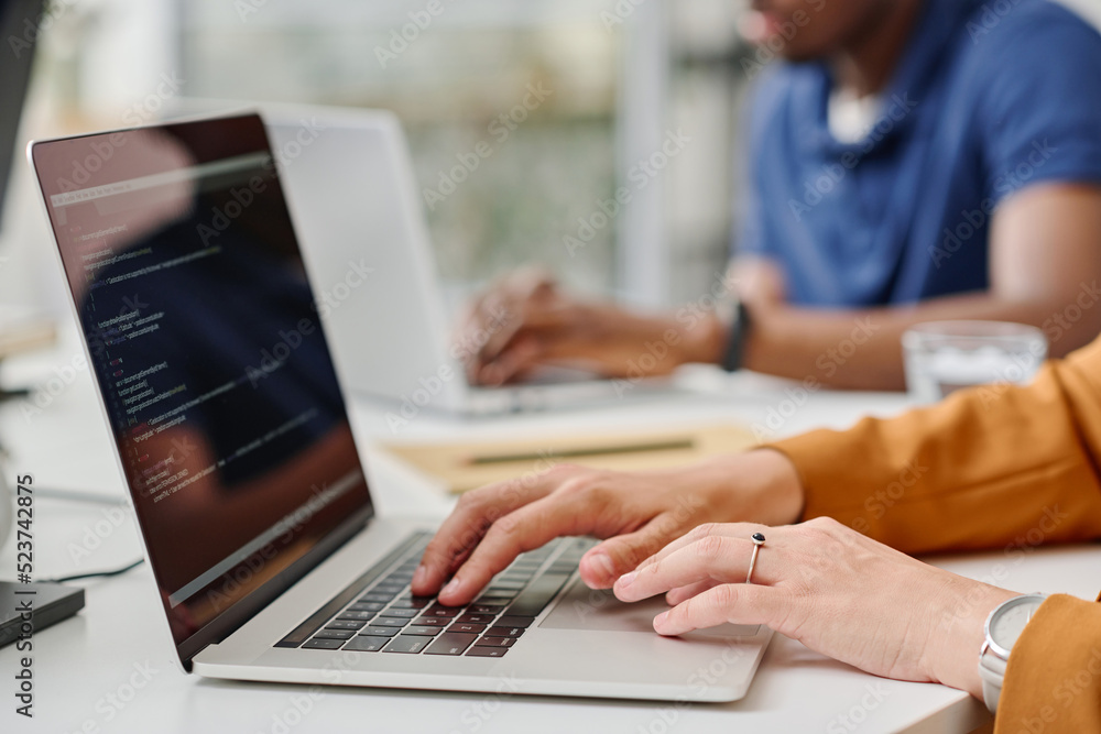 Close -up of female programmer typing codes on laptop during her work at office with colleagues Close -up of female programmer typing codes on laptop during her work at office with colleagues