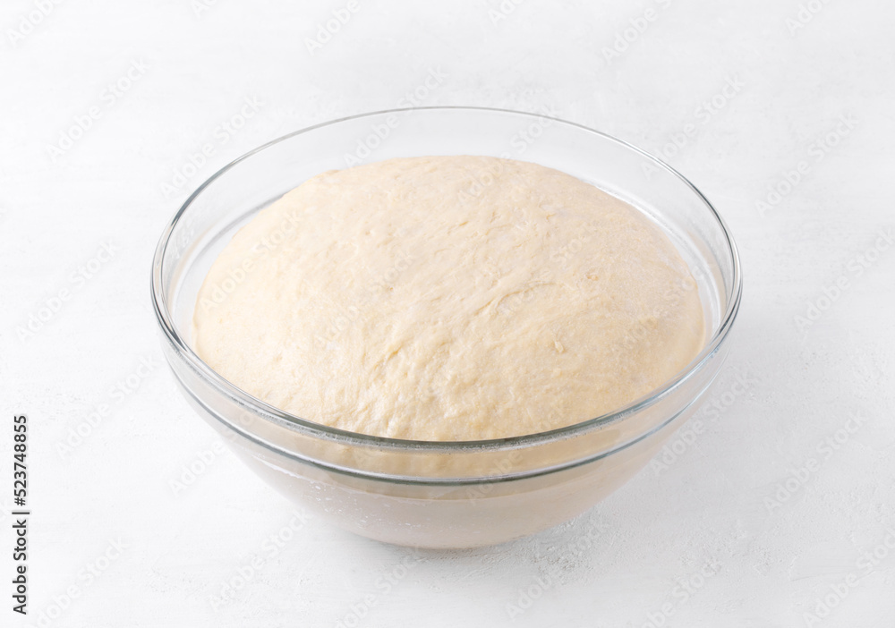 Yeast dough rising in glass bowl on white table. Proofing baking technique