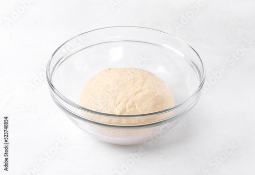Yeast dough in glass bowl on white table. Proofing baking technique