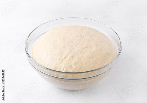 Yeast dough rising in glass bowl on white table. Proofing baking technique