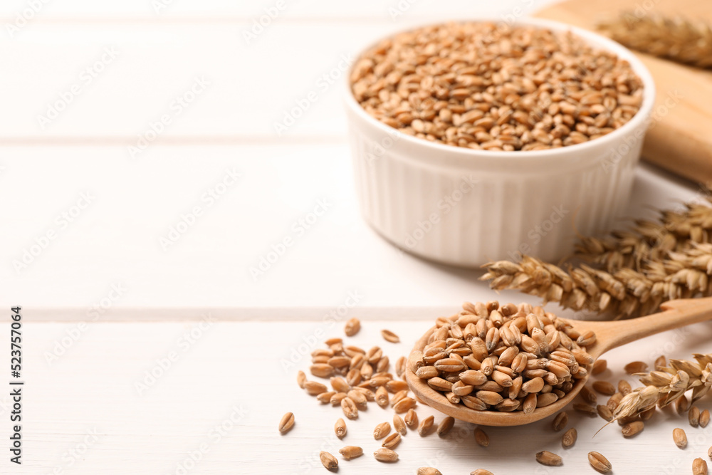 Wheat grains on white wooden table, space for text Wheat grains on white wooden table, space for text