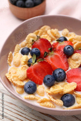 Bowl of tasty crispy corn flakes with milk and berries on white wooden table, closeup