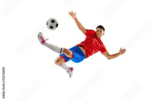 Portrait of young man, football player in motion, training, kicking ball in jump isolated over white studio background