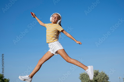 Happy girl jumping while listening to music in park