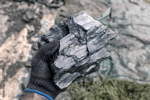 Piece of coal in a man's hand on a blurred background. Energy and fuel industry. The miner shows the volcanic rock.