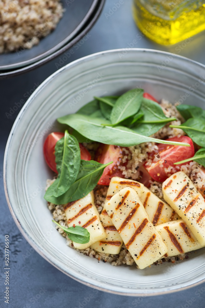 Grey plate with quinoa, grilled haloumi, fresh spinach and tomato salad, vertical shot, close-up Grey plate with quinoa, grilled haloumi, fresh spinach and tomato salad, vertical shot, close-up