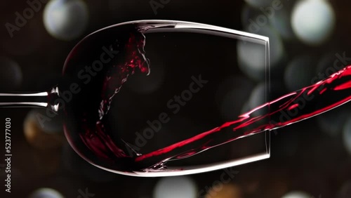 Red wine pouring into bordo glass in slow motion vertical shot. Alcohol on christmas bokeh background
