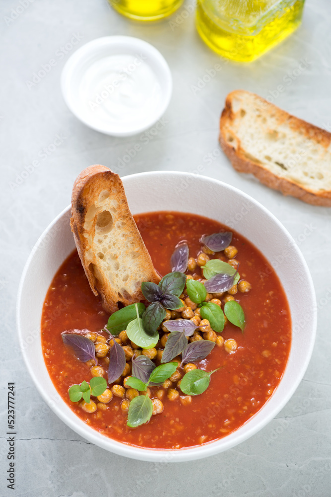 Bowl of tomato soup with roasted chickpeas and basil on a light-grey stone background, vertical shot, elevated view Bowl of tomato soup with roasted chickpeas and basil on a light-grey stone background, vertical shot, elevated view