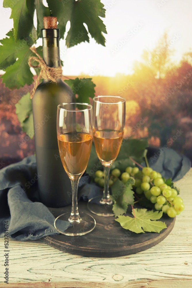 Glasses of white wine, a bunch of grapes on a wooden table, against the backdrop of sunset, romantic atmosphere, harvest, natural products